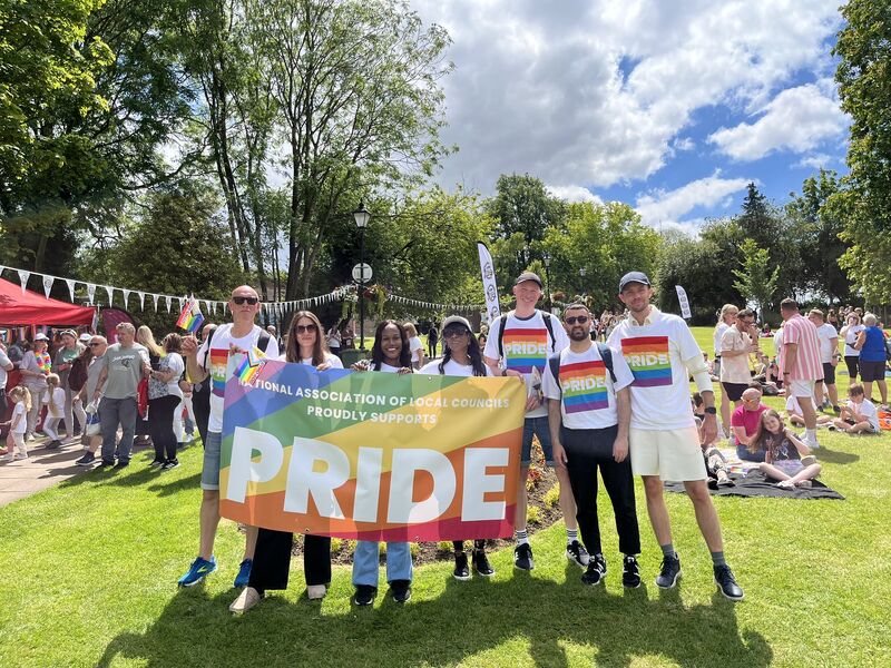 Staff of NALC and KALC standing next to a Pride flag on a sunny day at a pride parade